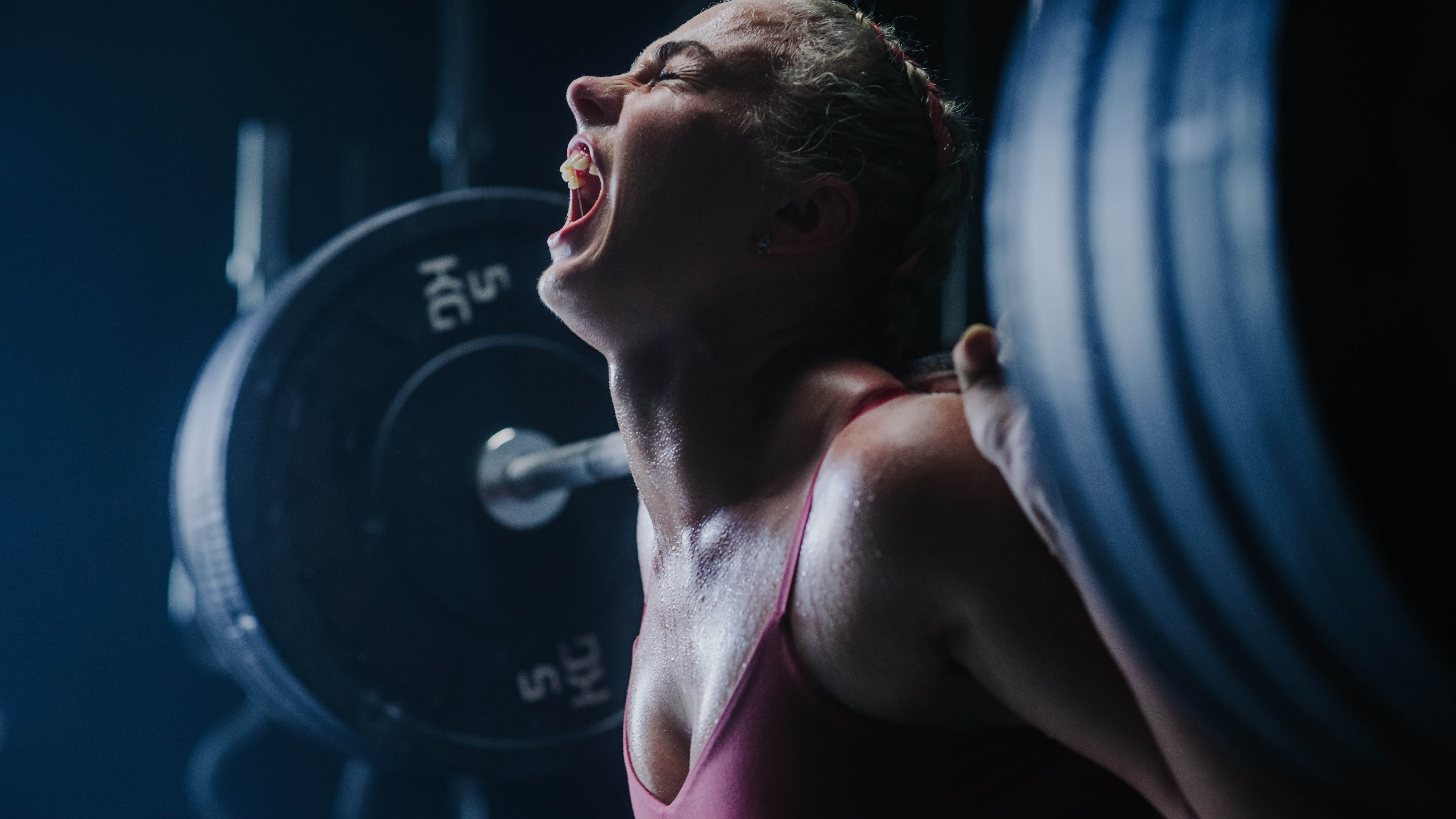 Woman yelling with exhaustion with a heavy barbell of weights on her shoulders